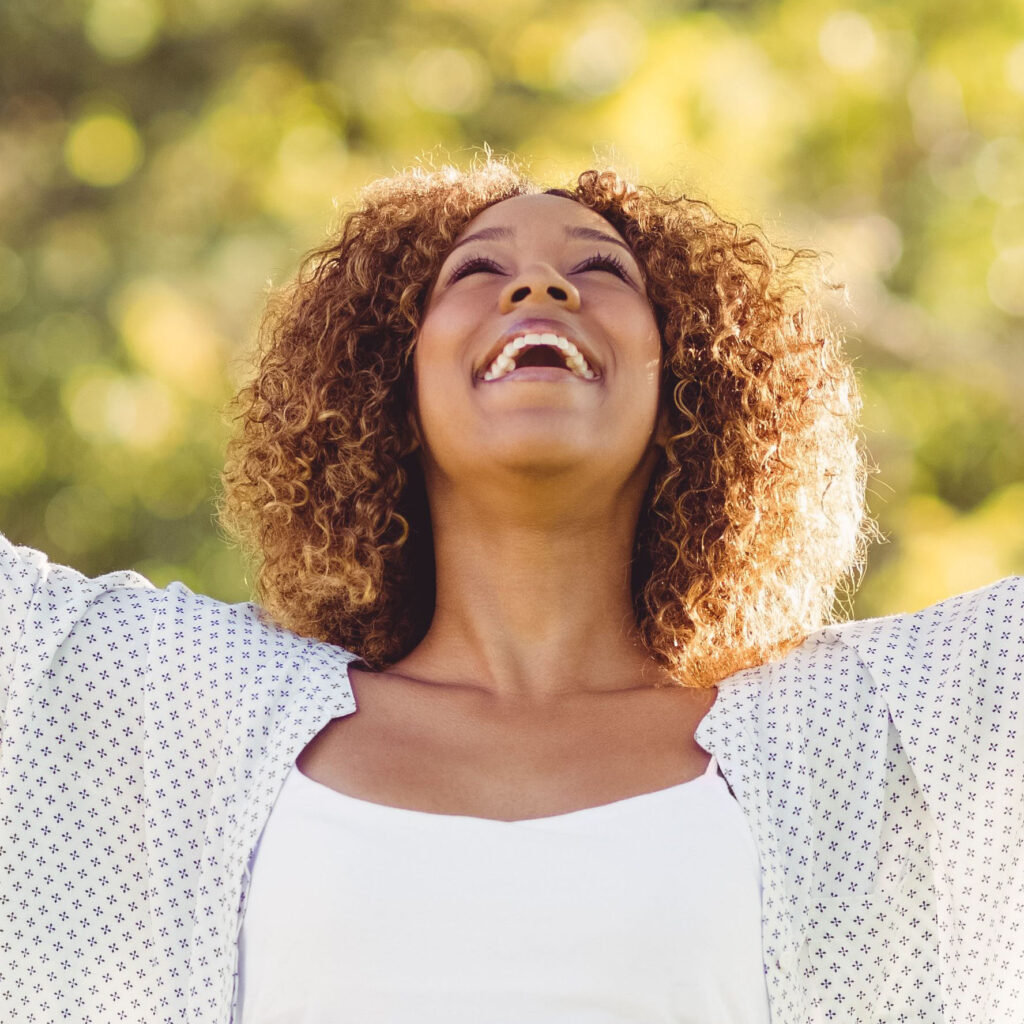A joyful woman with curly hair smiles with her arms outstretched, representing client satisfaction with our web design servic